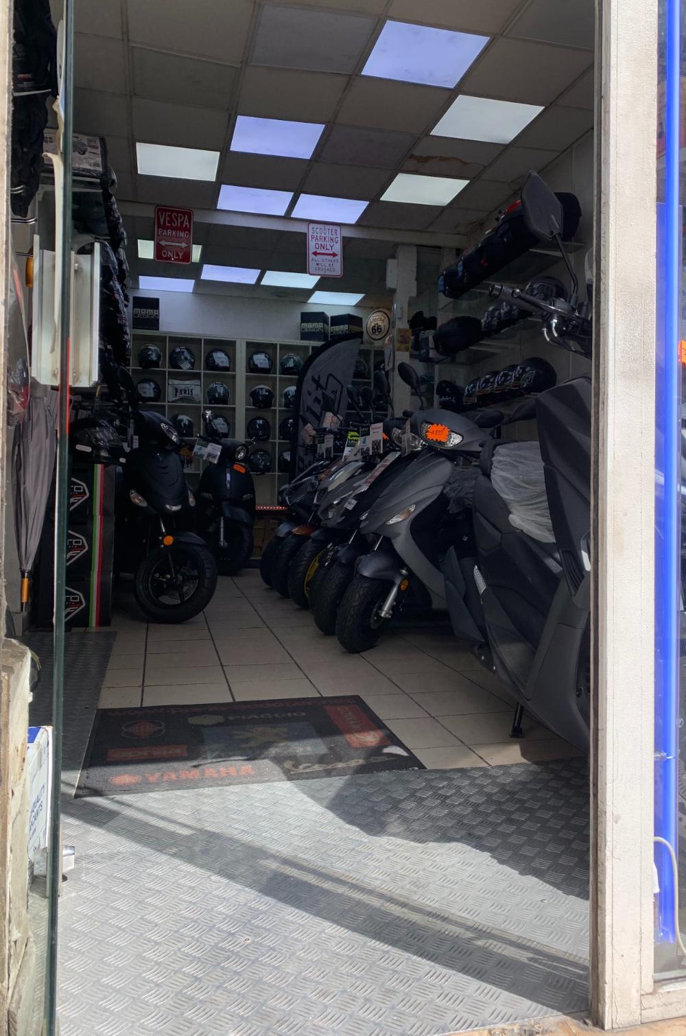L'entrée du magasin vue du trottoir, avec les scooters en rang