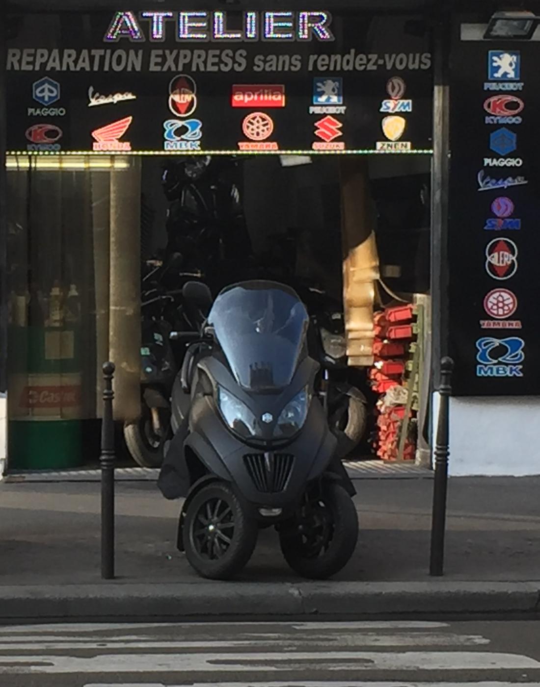 La façade de l'atelier Paris Scooter, avec l'inscription Réparation express sans rendez-vous et un scooter trois roues garé devant